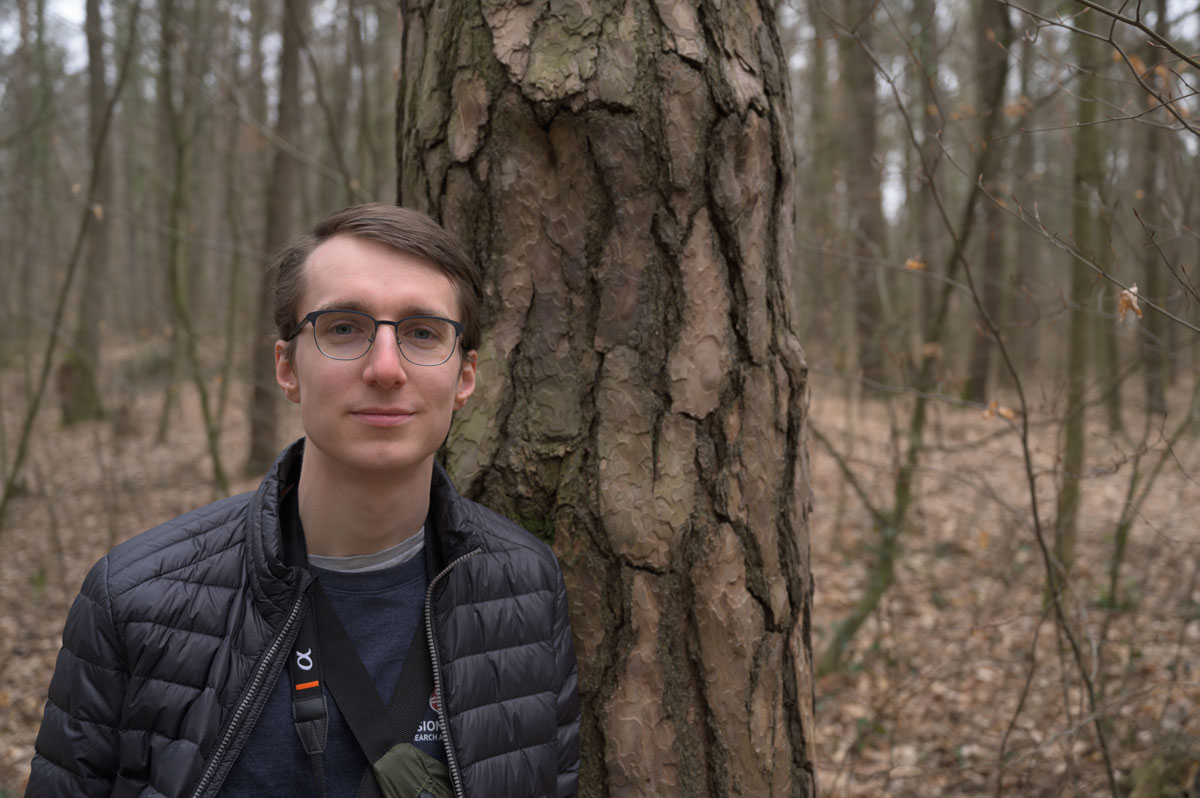 Portrait des Grafikdesigners Konrad Hauswald im herbstlichen Wald (Dresdener Heide). Er lehnt an einem Baum und schaut frontal in die Kamera.